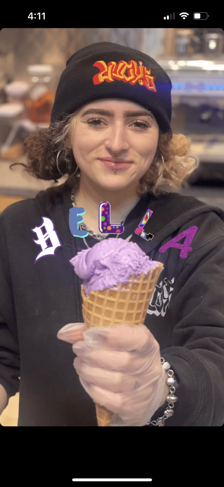 Young woman holding a purple ice cream cone, wearing a black beanie and jacket, smiling outdoors.