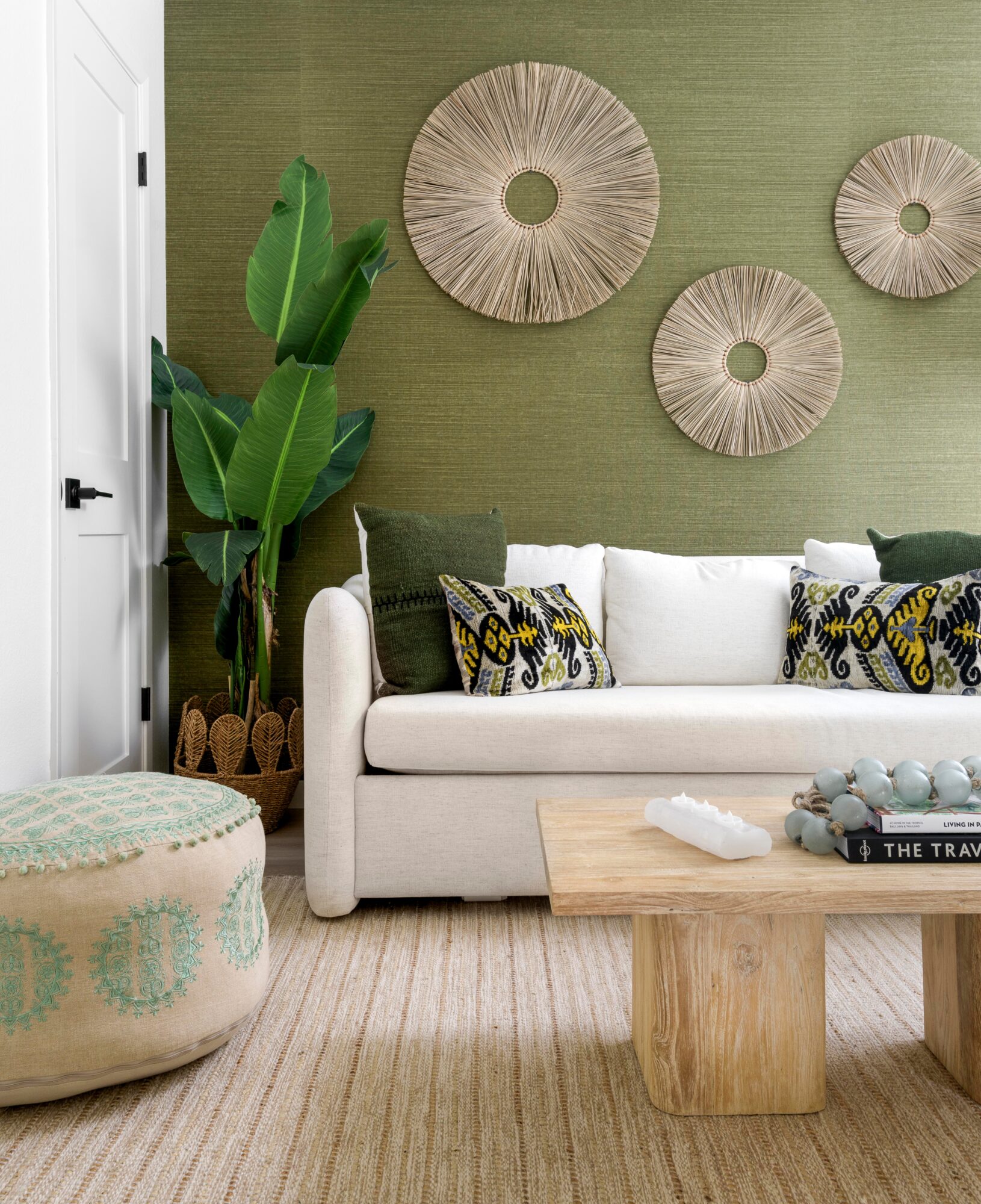 Living room with white sofa, green wall, wall art, large plant, and wooden coffee table.