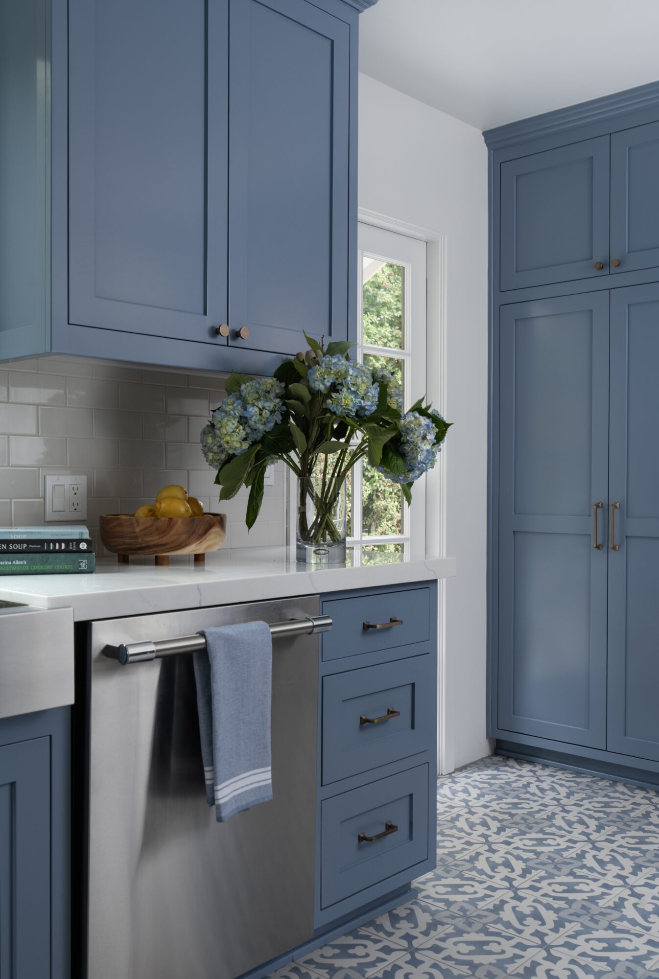 Blue kitchen cabinets with a window, a vase of flowers, and a towel hanging on a drawer handle.