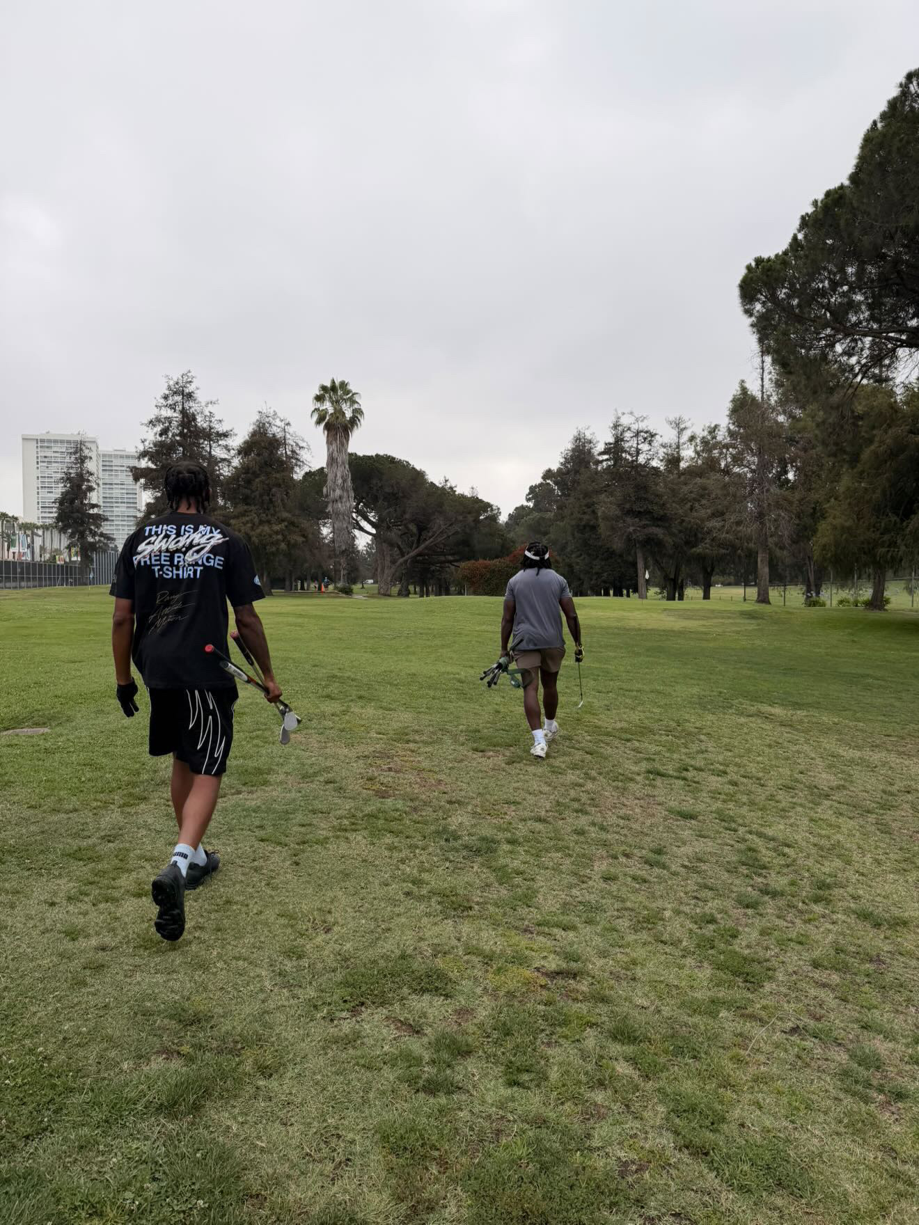 Two people walking on a grassy field with trees and cloudy sky in the background.