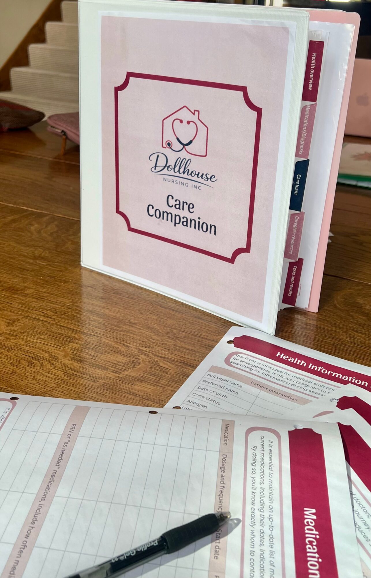 Care companion booklet with tabs on a wooden surface, partially open, with a pen and a sheet of paper nearby.