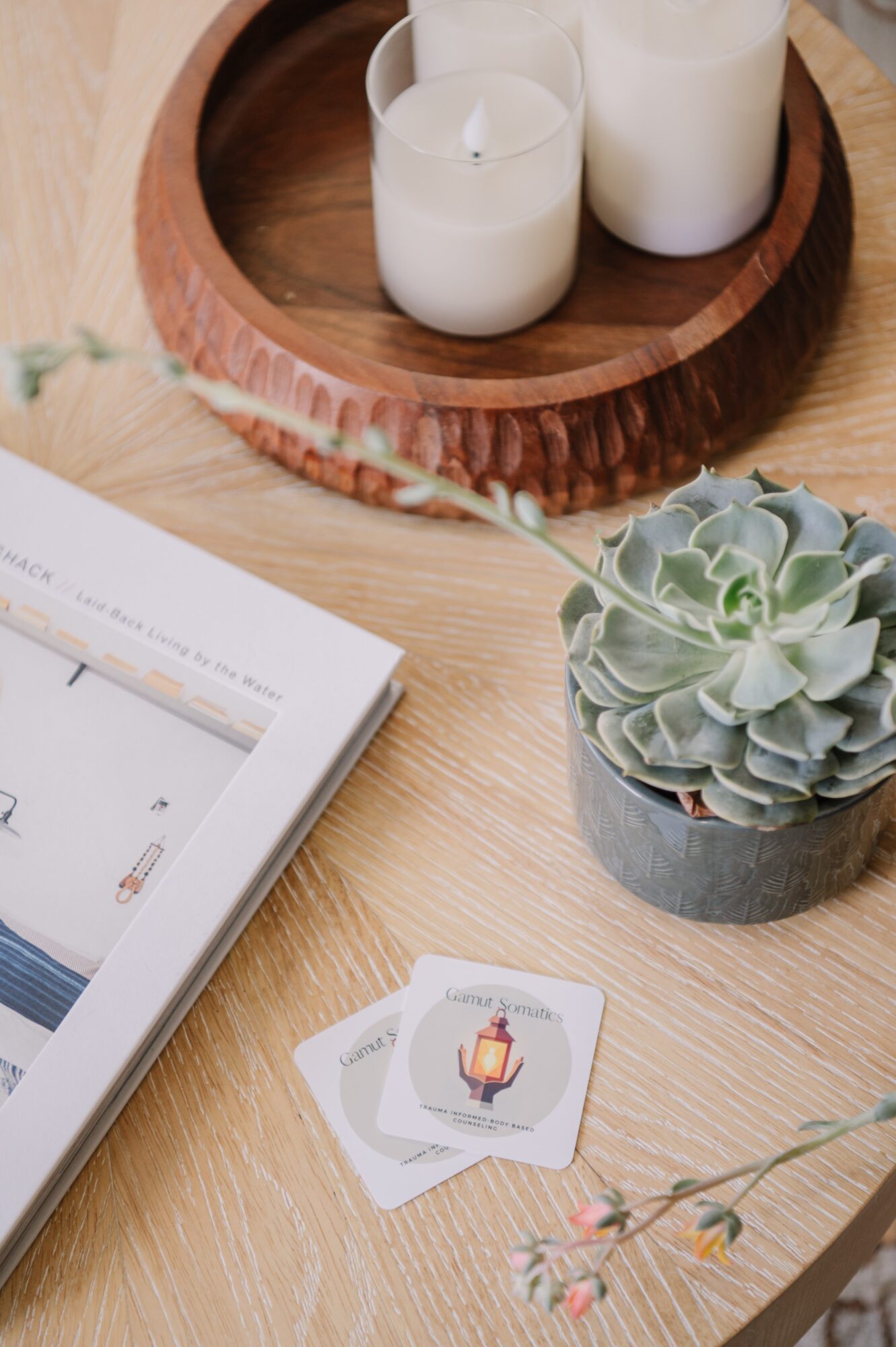 Wooden tray with three white candles, a potted succulent plant, and a magazine on a wooden surface.