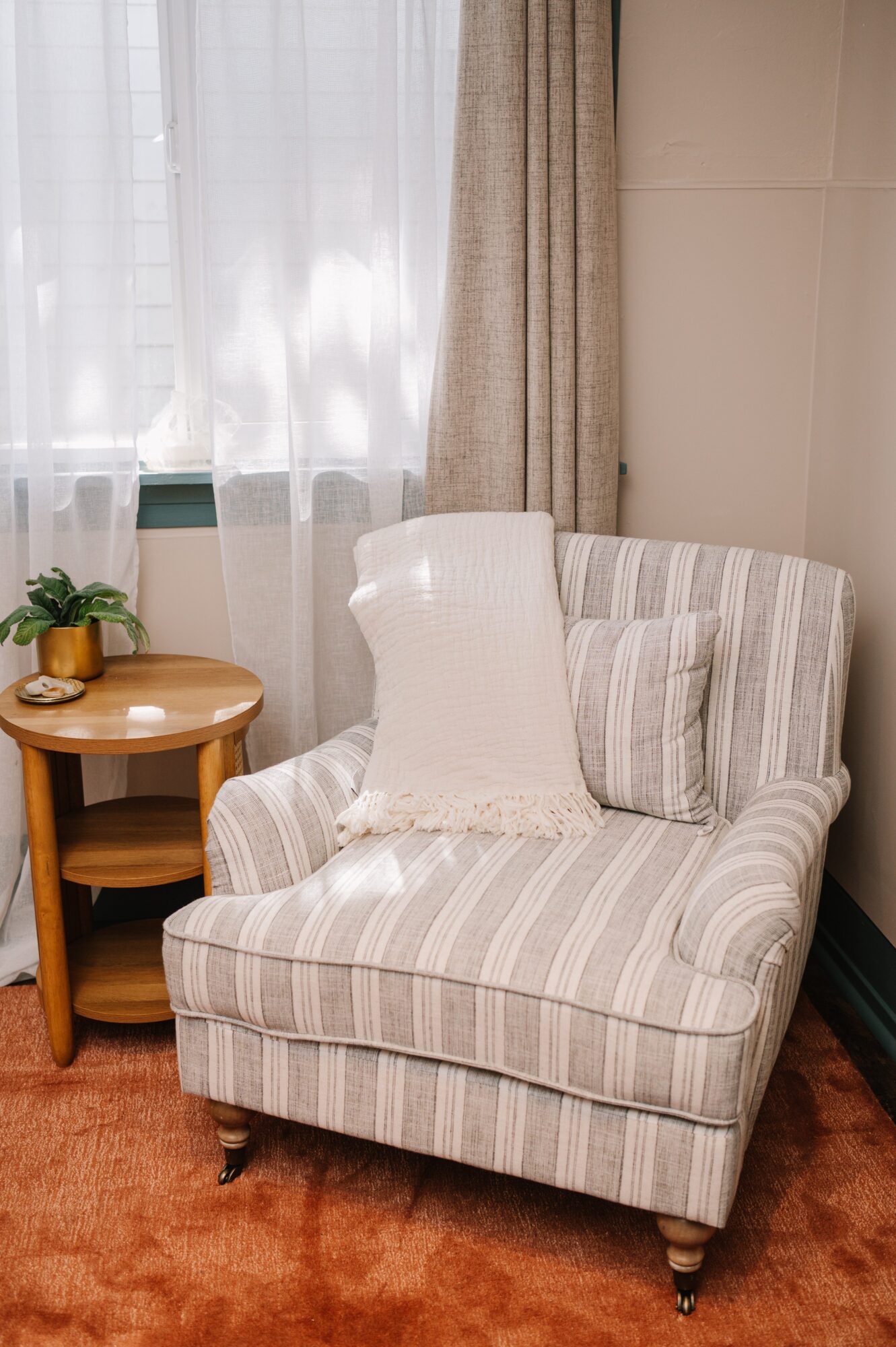 Upholstered armchair with striped fabric, a pillow, next to a small wooden side table with a plant, in a cozy room.