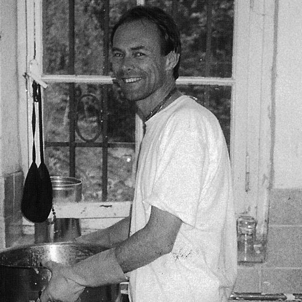 Man smiling washing dishes in kitchen with window behind him, black and white photo.