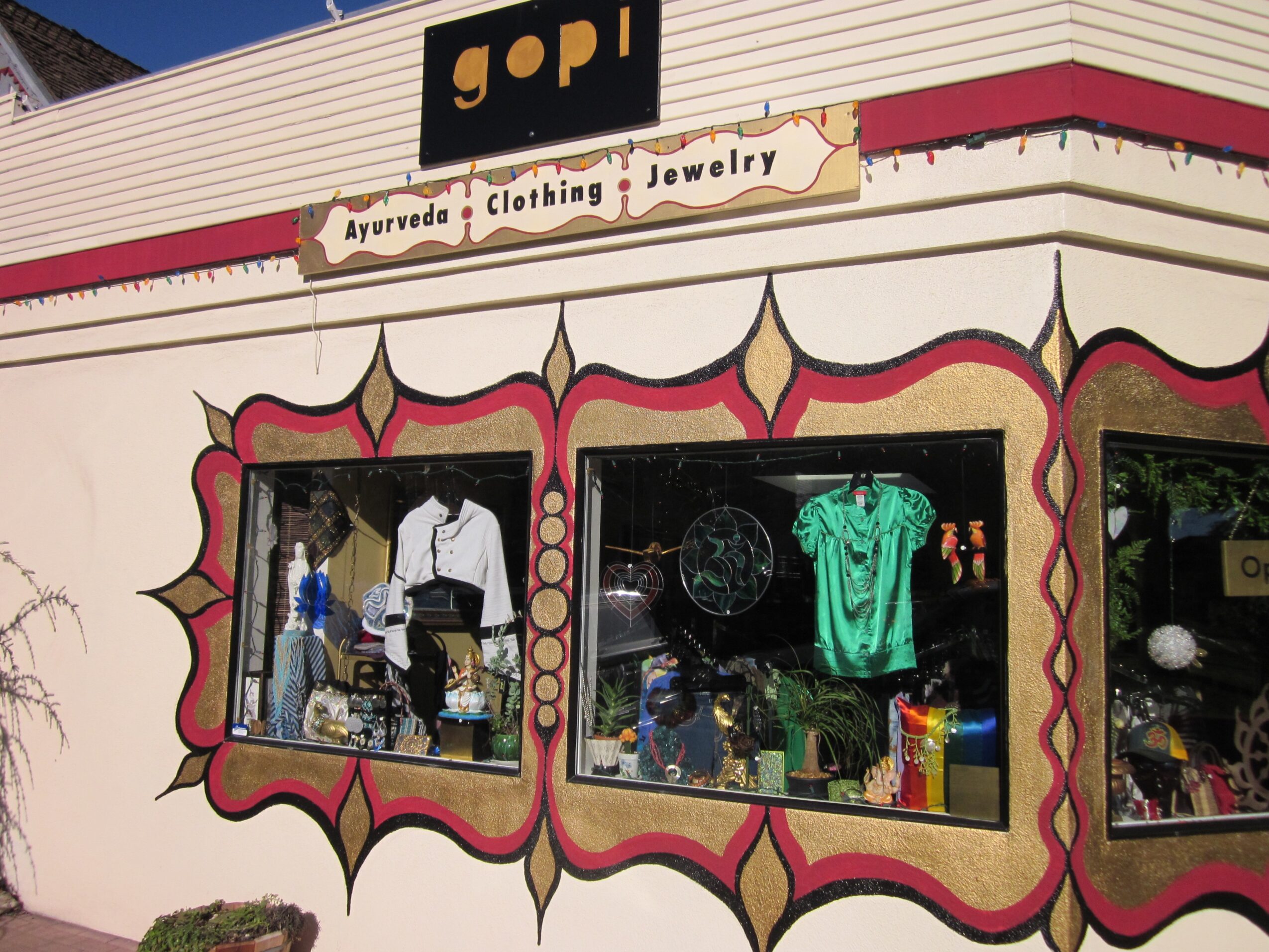 Storefront with three large display windows showing clothing and jewelry, decorative trim, and a sign reading 'gopi' above.