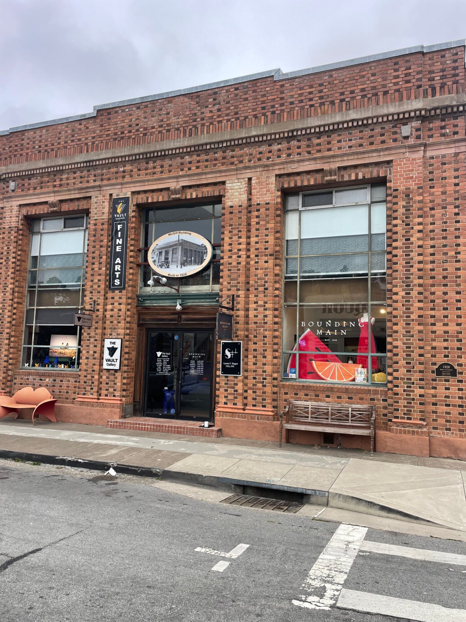 Brick building with large windows and a door, street with crosswalk, overcast sky, and a sign with a red umbrella.