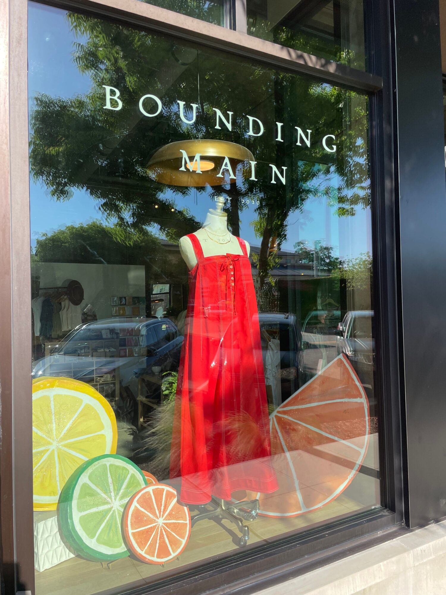 Store window display with a red dress and citrus fruit illustrations, and text reading 'BOUNDED IN NAIN'.