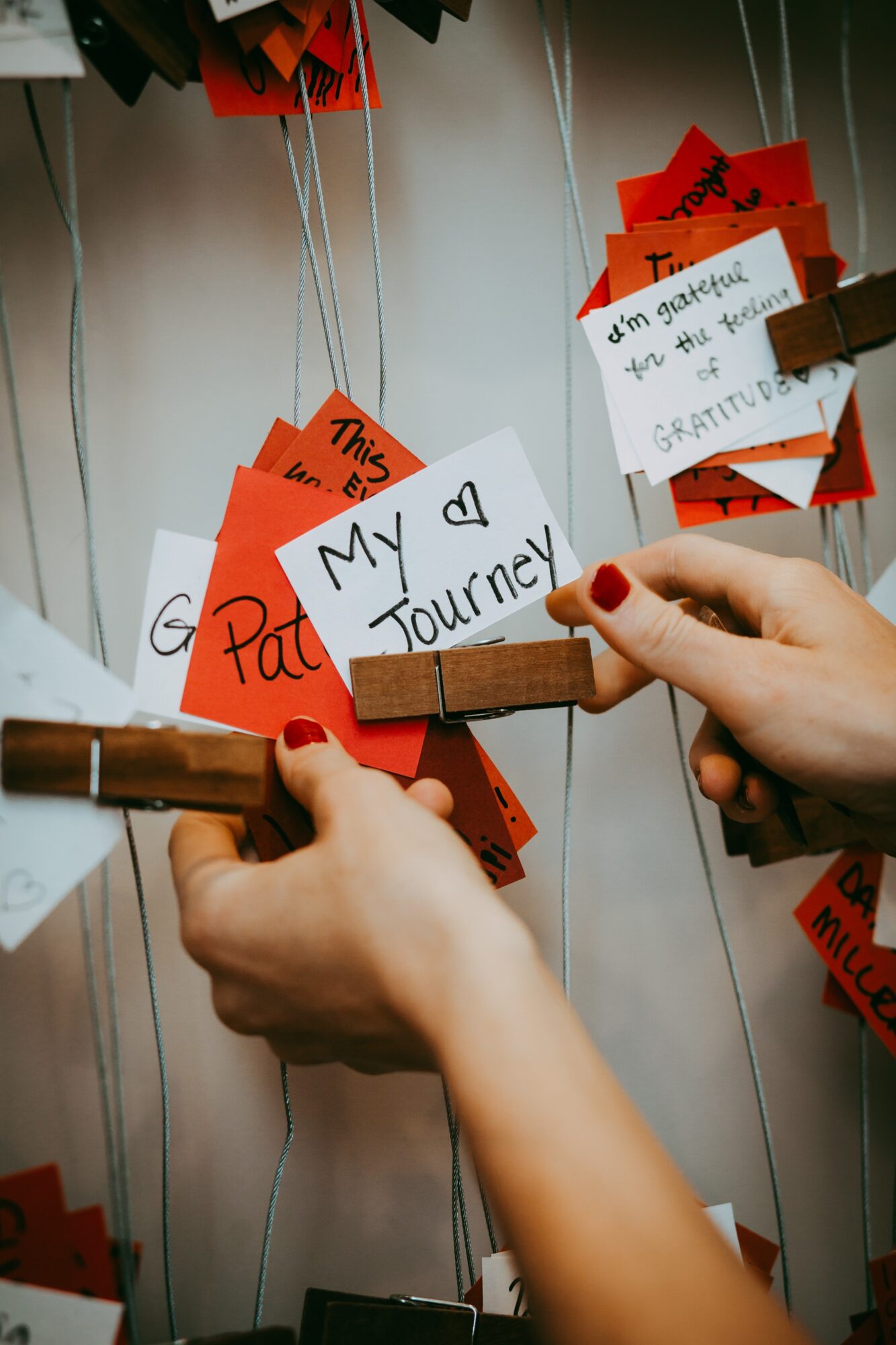 Hands pinning a paper heart labeled 'My ♥️ Path to a Journey' among red and white notes on a wall.