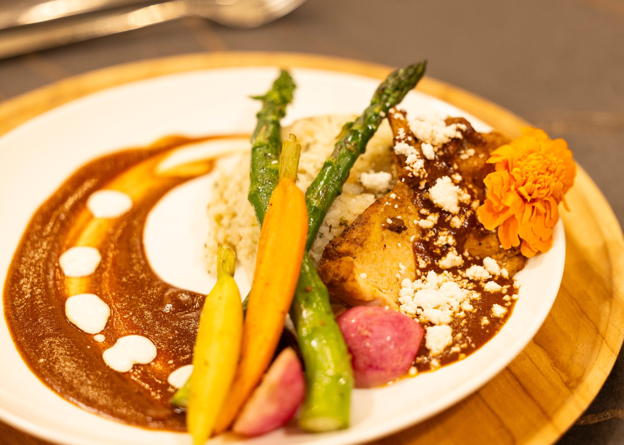 Plate with asparagus, mashed potatoes, sauce, and a flower garnish, served on a wooden tray.