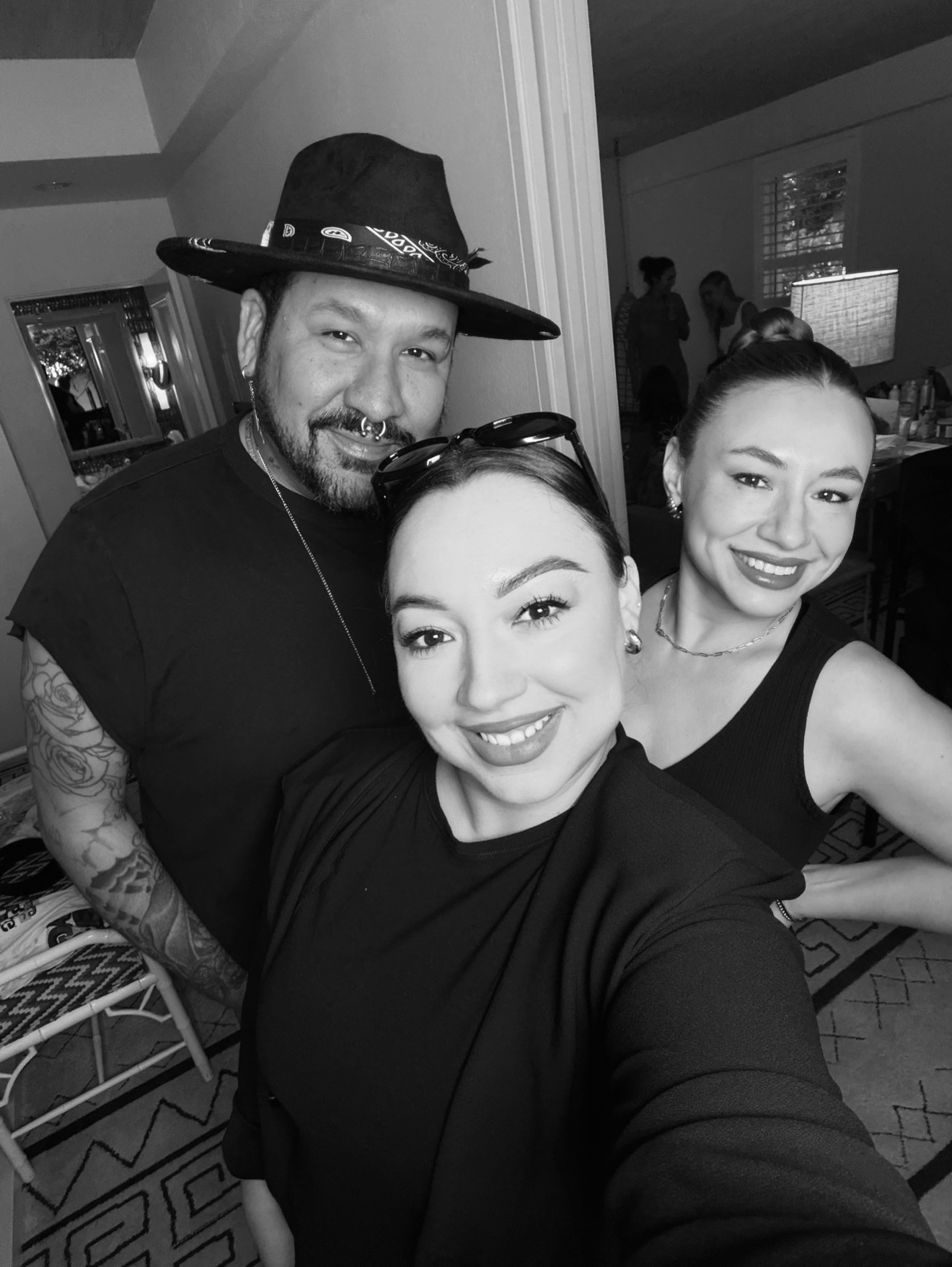 Three people smiling, two women and one man, in a room with a television and furniture, black and white photo.