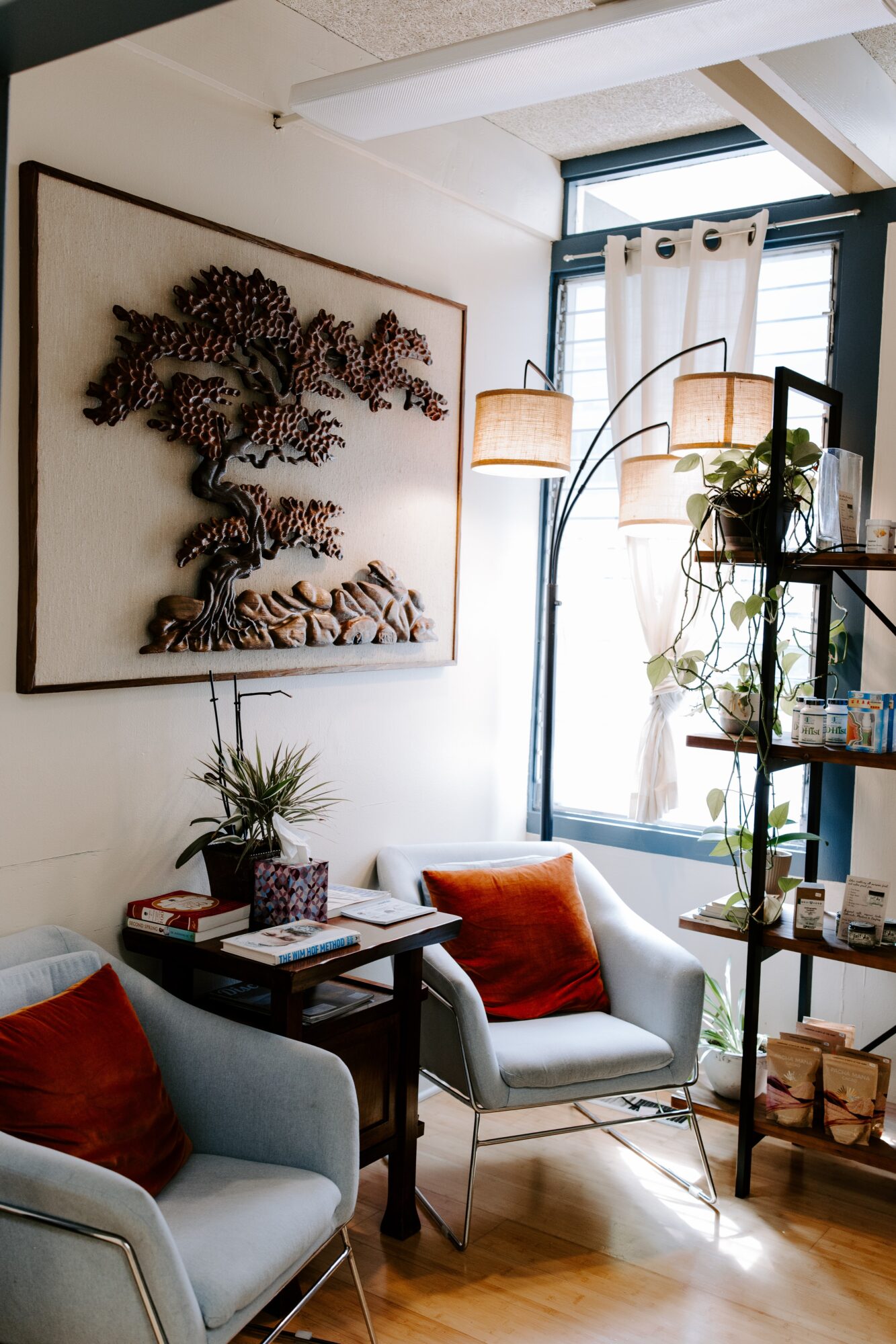 Living room with a large wall art of a tree, two armchairs with cushions, a small table, and a window with curtains.