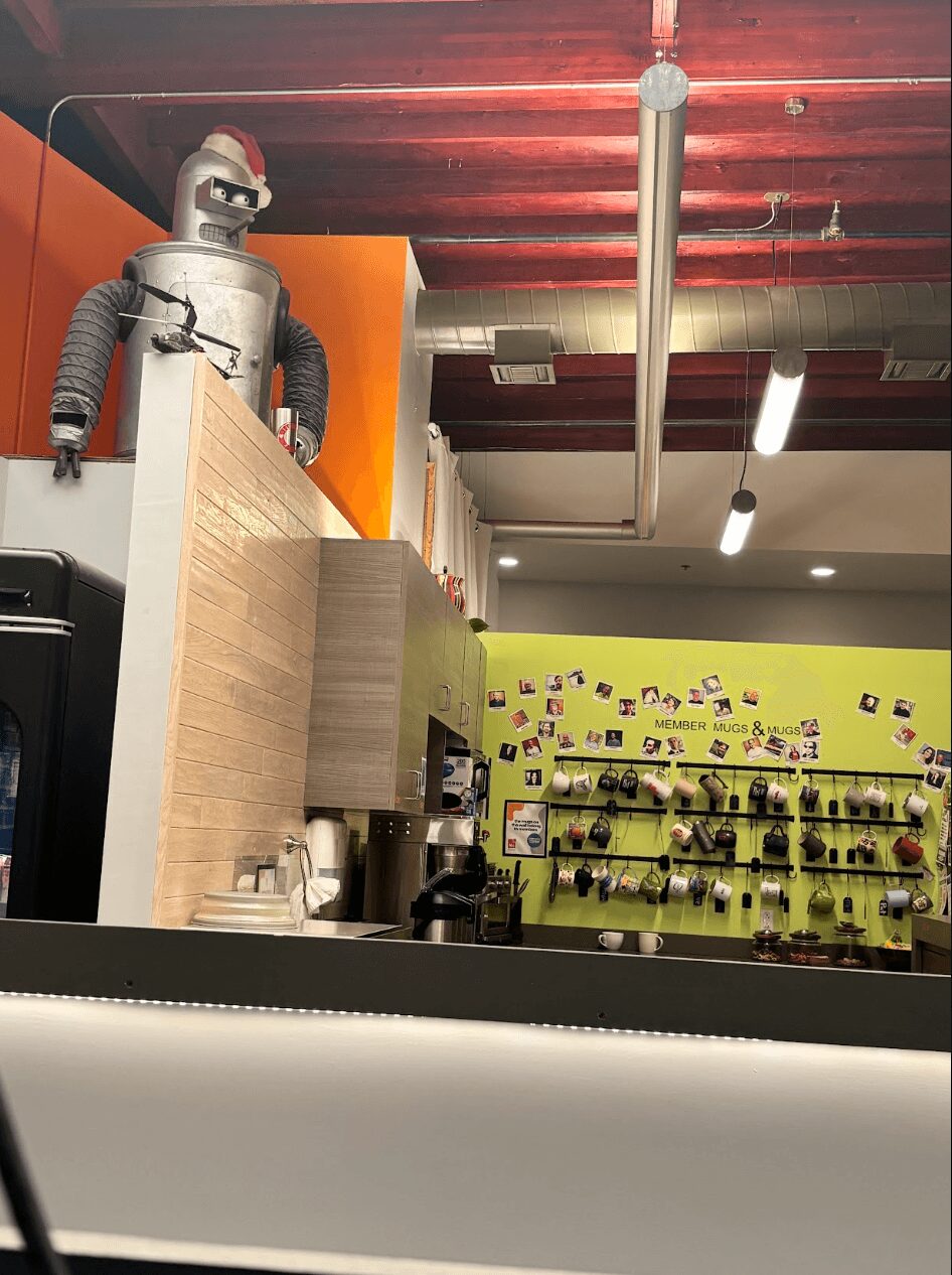 Robot figure with sunglasses and Santa hat on a shelf in a store, with shelves and products in the background.
