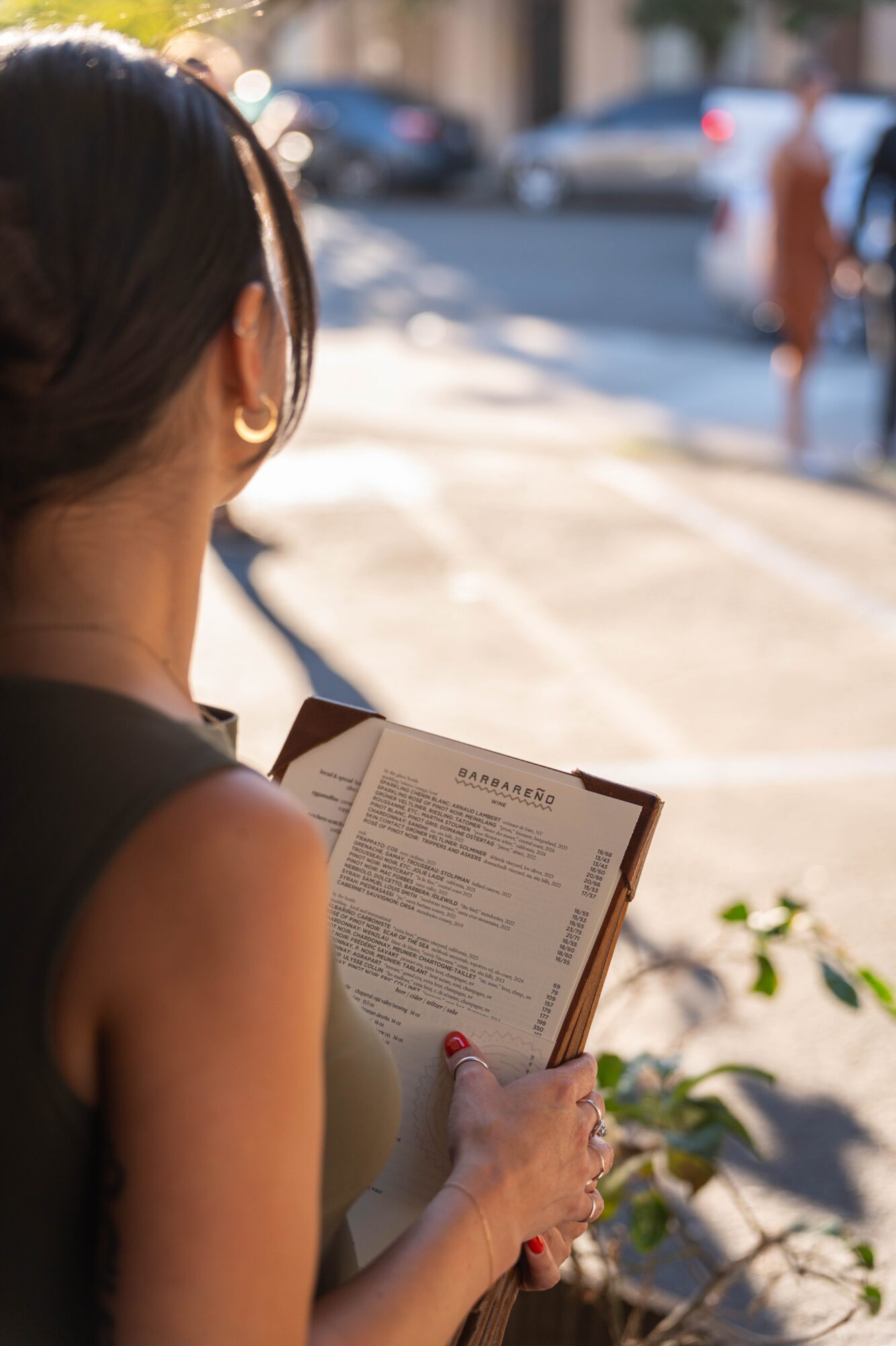 Person reading a menu outdoors with blurred street scene in background.