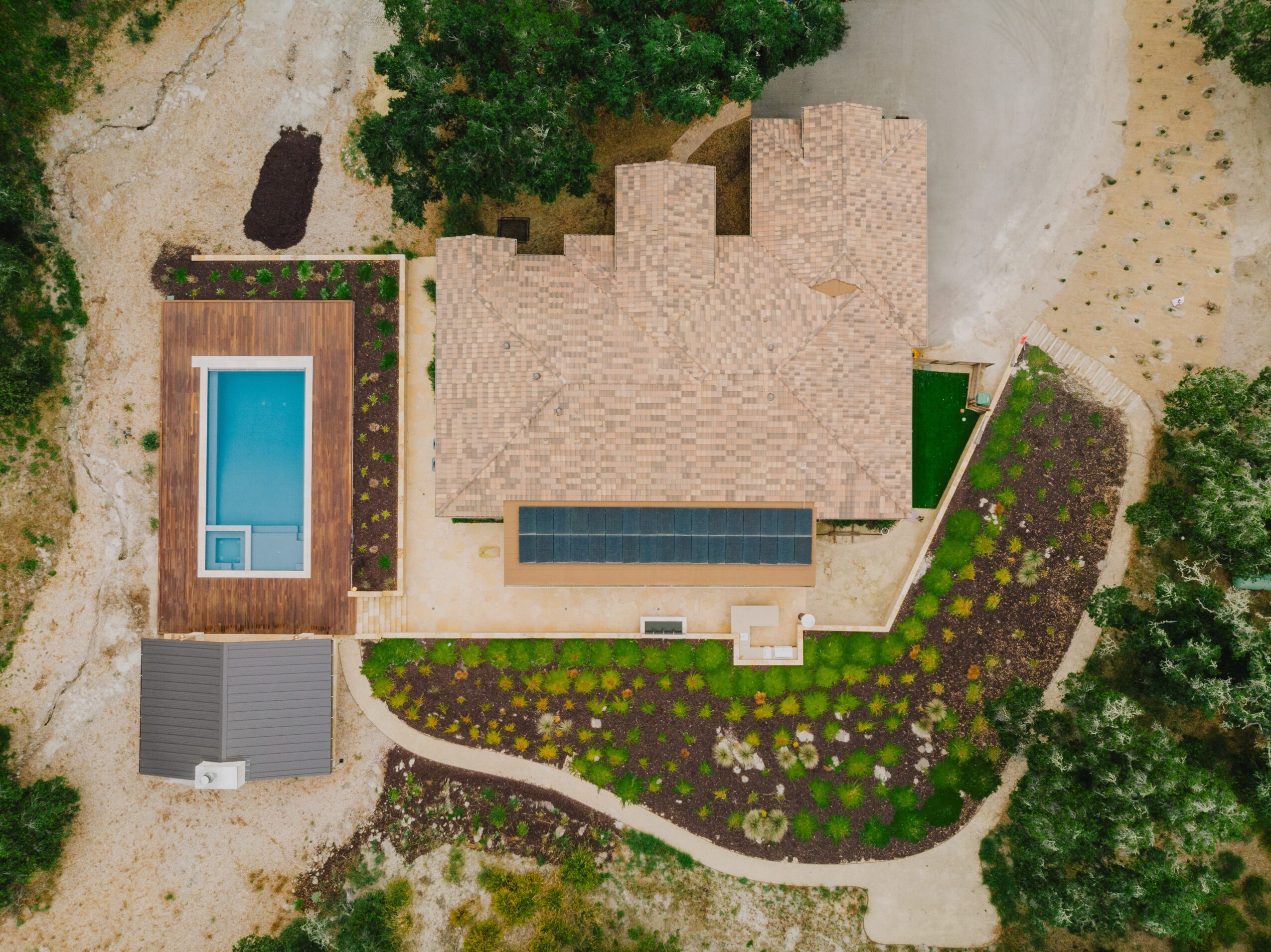 A house with a backyard pool, garden, driveway, and surrounding trees, viewed from above.